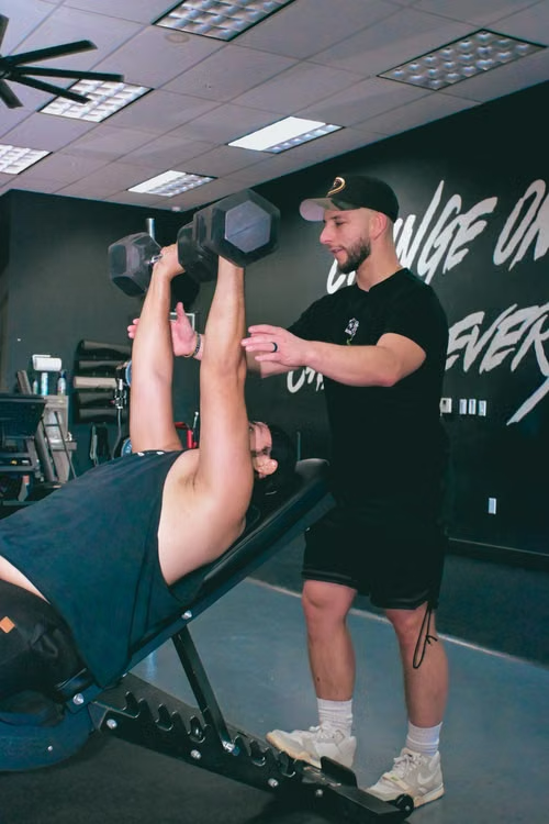 Coach guiding a client through a dumbbell press
